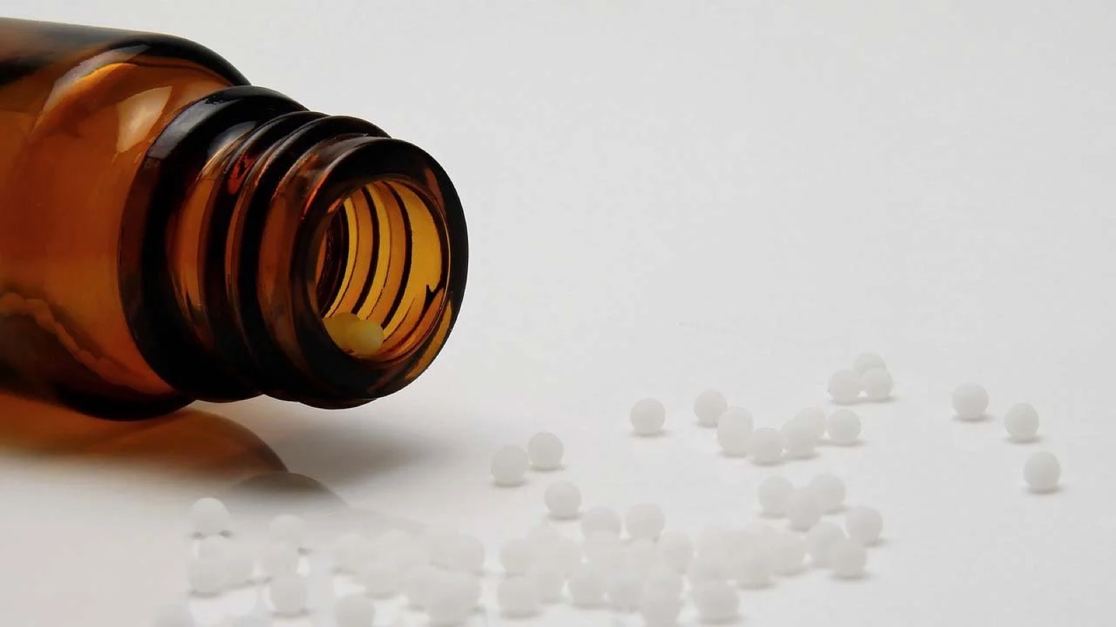 Brown glass bottle lying on its side, with white tablets falling out of the opening.