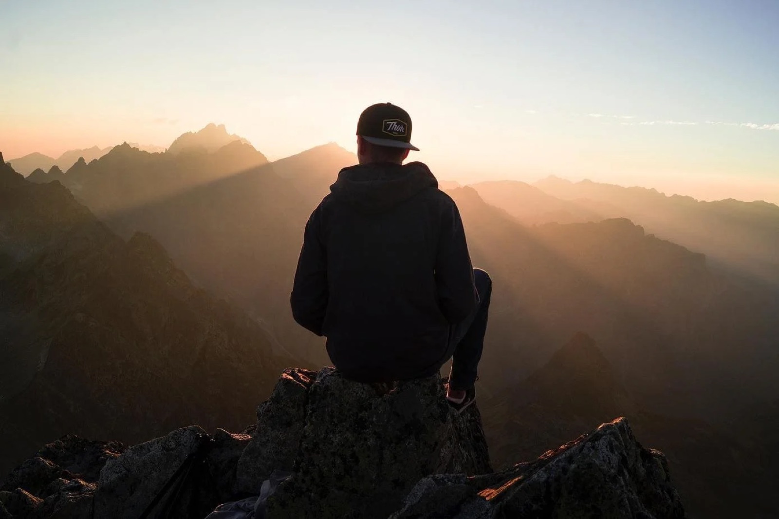 Person sitting on a rock looking at the mountains and the sunset.