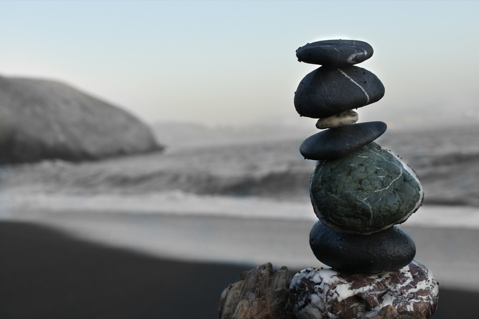 Stones stacked on a rock on a beach, with the sea and a rock in the background