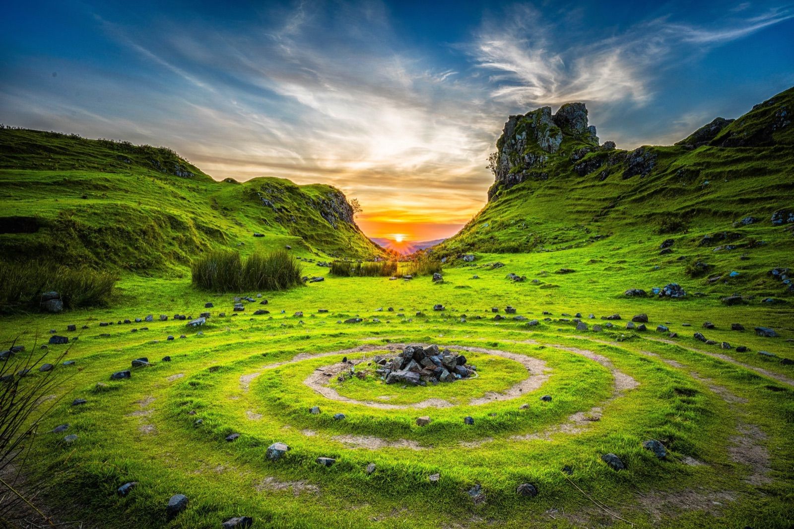 Sunset over green hills with rocks, grass and a stone circle in a riverbed