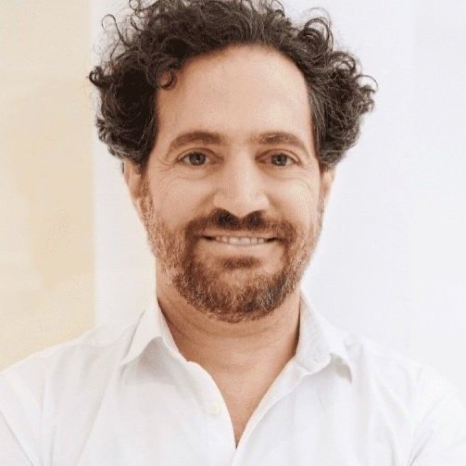 Portrait of a smiling man with dark, curly hair, a beard and a white shirt.